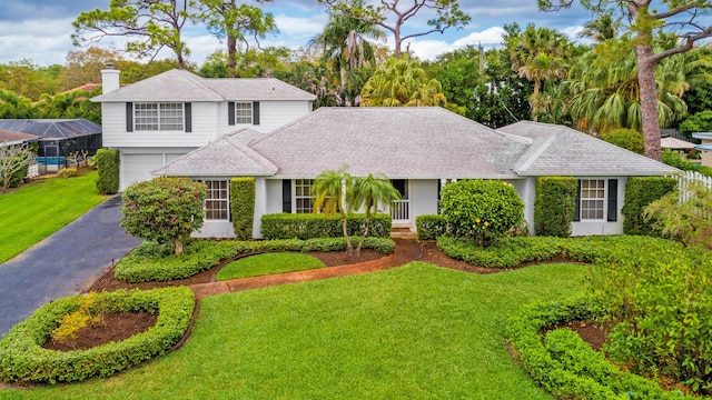 view of front facade with roof with shingles, a chimney, a front lawn, a garage, and aphalt driveway