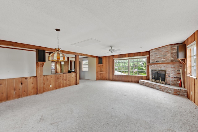 unfurnished living room with a textured ceiling, wooden walls, a fireplace, and carpet