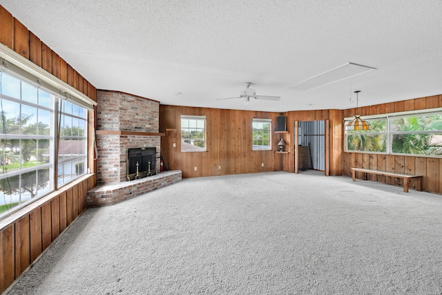 unfurnished living room with attic access, a fireplace, wood walls, a textured ceiling, and light carpet