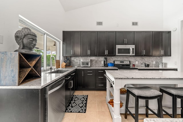 kitchen featuring sink, stainless steel appliances, high vaulted ceiling, light stone countertops, and decorative backsplash