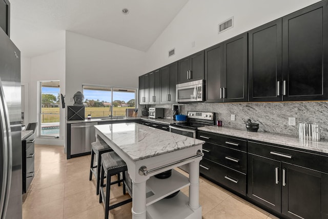 kitchen with a kitchen bar, a center island, appliances with stainless steel finishes, light stone countertops, and decorative backsplash