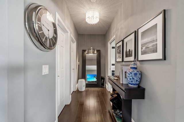 corridor featuring dark wood-type flooring, a notable chandelier, and a textured ceiling