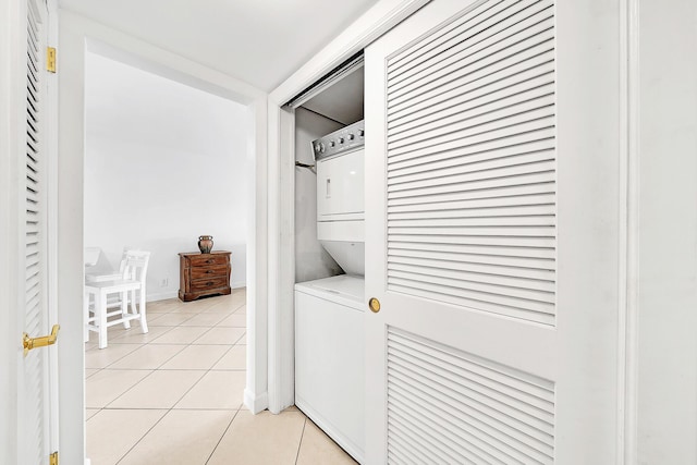 clothes washing area with light tile patterned floors, baseboards, laundry area, and stacked washer / drying machine