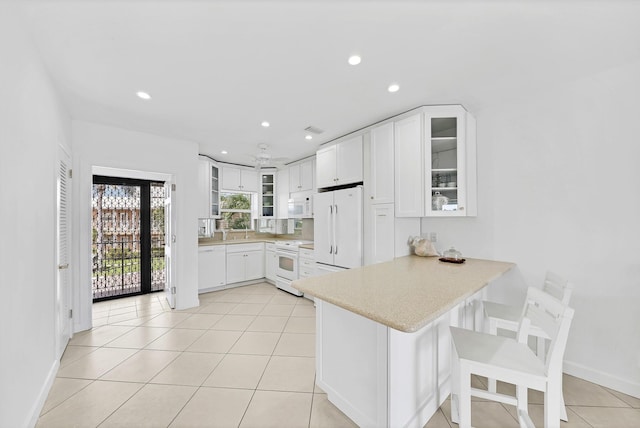 kitchen featuring a breakfast bar, white appliances, glass insert cabinets, and light countertops