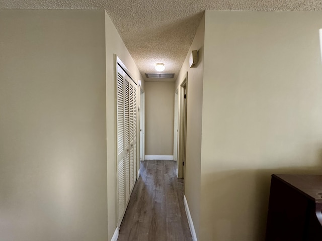 corridor with a textured ceiling and dark wood-type flooring