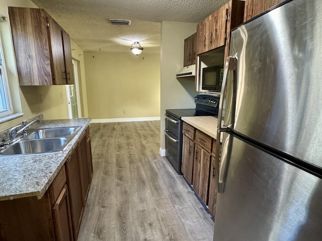 kitchen featuring light wood-type flooring, double oven range, stainless steel refrigerator, sink, and a textured ceiling