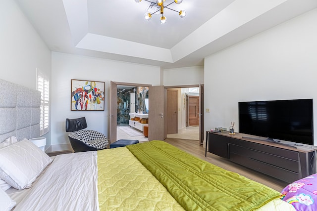 bedroom featuring a tray ceiling, a chandelier, wood finished floors, and ensuite bathroom