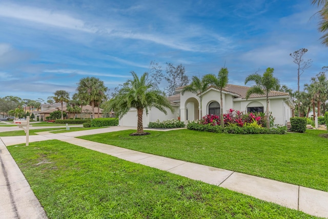 mediterranean / spanish-style house featuring a tile roof, stucco siding, concrete driveway, an attached garage, and a front lawn