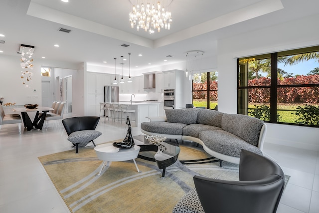 living room featuring a tray ceiling, sink, and an inviting chandelier