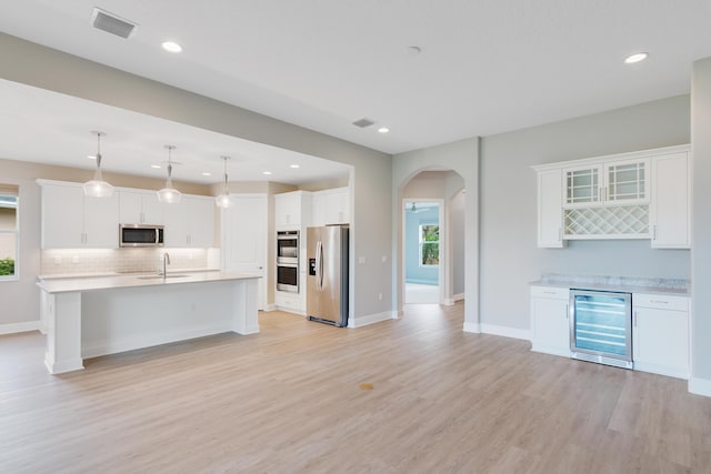 kitchen featuring arched walkways, light countertops, appliances with stainless steel finishes, a sink, and beverage cooler