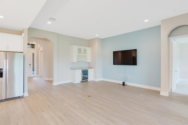 unfurnished living room with arched walkways, wine cooler, a dry bar, visible vents, and light wood finished floors