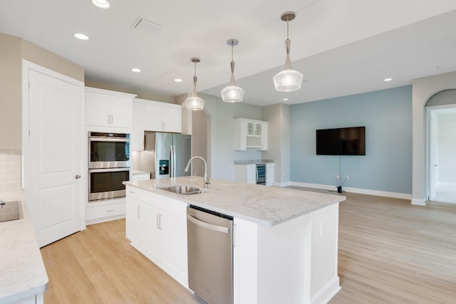 kitchen featuring a center island with sink, stainless steel appliances, light wood-type flooring, white cabinetry, and a sink