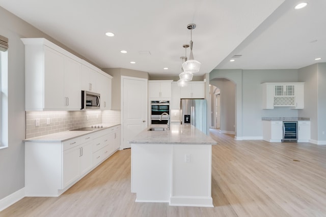 kitchen with arched walkways, stainless steel appliances, light wood-style floors, a sink, and beverage cooler