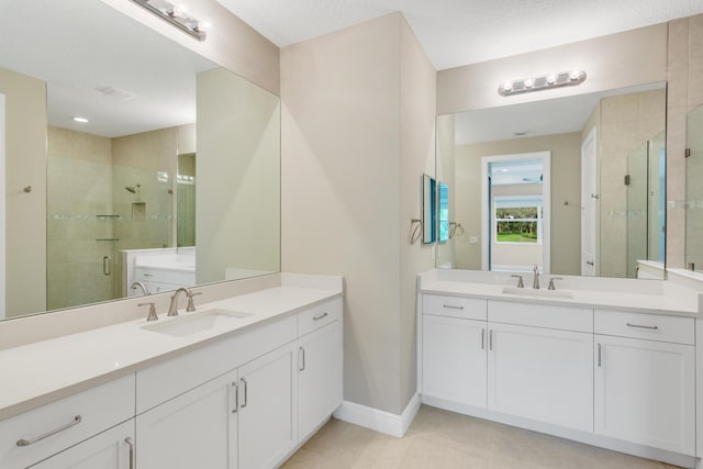 full bathroom featuring a stall shower, two vanities, a sink, and baseboards