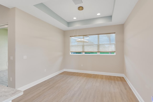 spare room featuring light wood finished floors, baseboards, visible vents, a raised ceiling, and recessed lighting