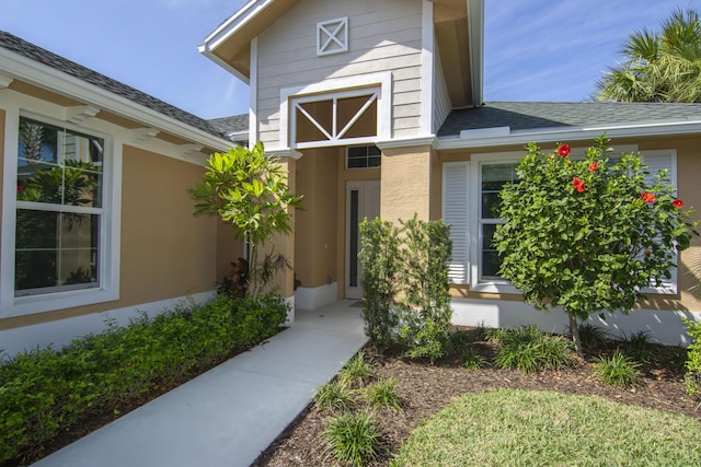 entrance to property with a shingled roof and stucco siding