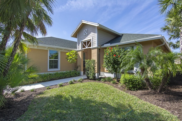 view of front of property featuring roof with shingles, a front lawn, and stucco siding