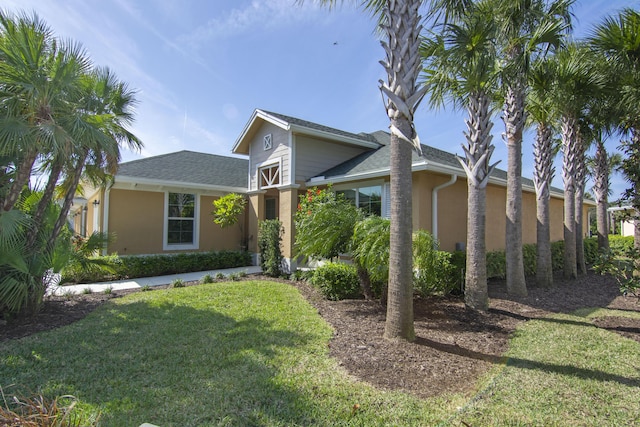 view of front of home featuring roof with shingles, a front lawn, and stucco siding