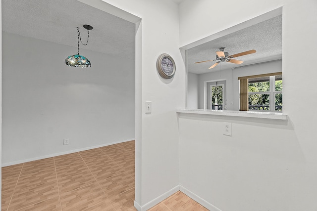 empty room with ceiling fan, a textured ceiling, and baseboards