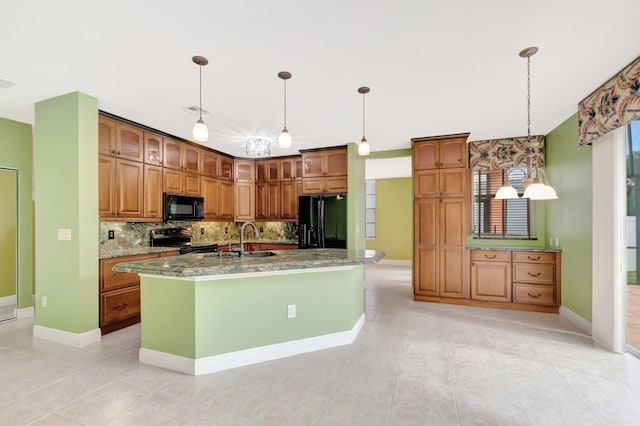 kitchen with decorative light fixtures, a sink, black appliances, brown cabinetry, and a center island with sink