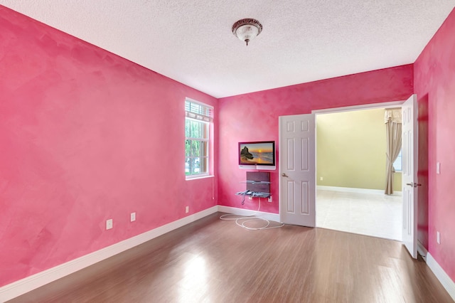 empty room featuring a textured ceiling, baseboards, and wood finished floors