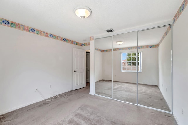 unfurnished bedroom with baseboards, visible vents, light colored carpet, a textured ceiling, and a closet