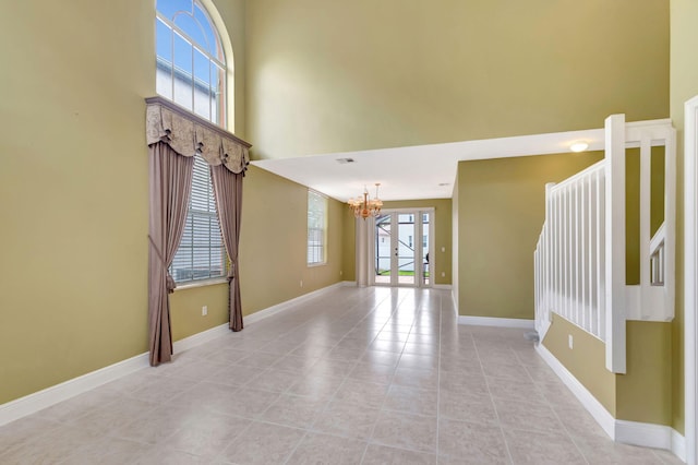 spare room with light tile patterned floors, visible vents, baseboards, a towering ceiling, and a notable chandelier