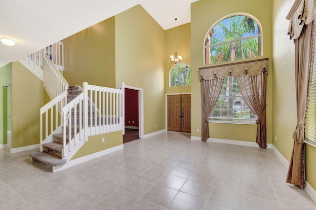 foyer entrance with stairs, a towering ceiling, baseboards, and an inviting chandelier