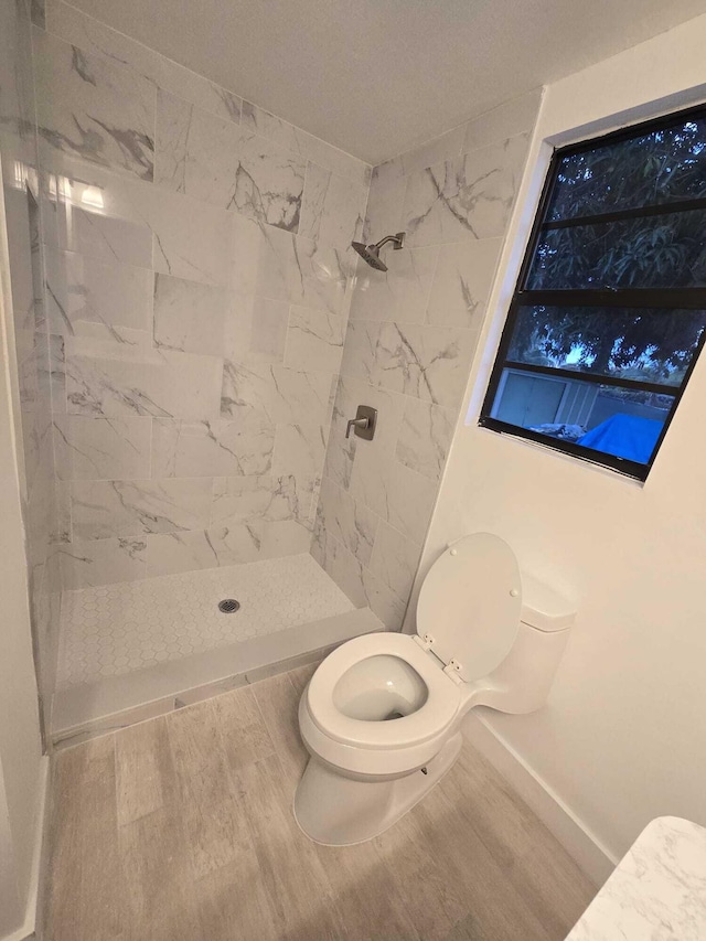 bathroom with a tile shower, wood-type flooring, and toilet