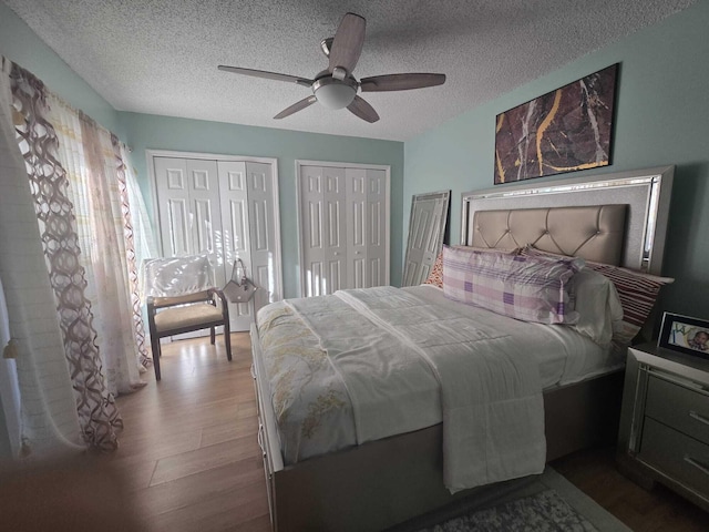 bedroom with multiple closets, ceiling fan, hardwood / wood-style floors, and a textured ceiling