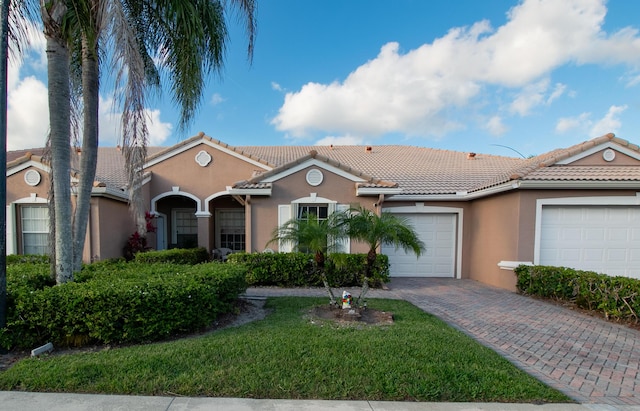 view of front facade featuring an attached garage, a tiled roof, decorative driveway, stucco siding, and a front yard