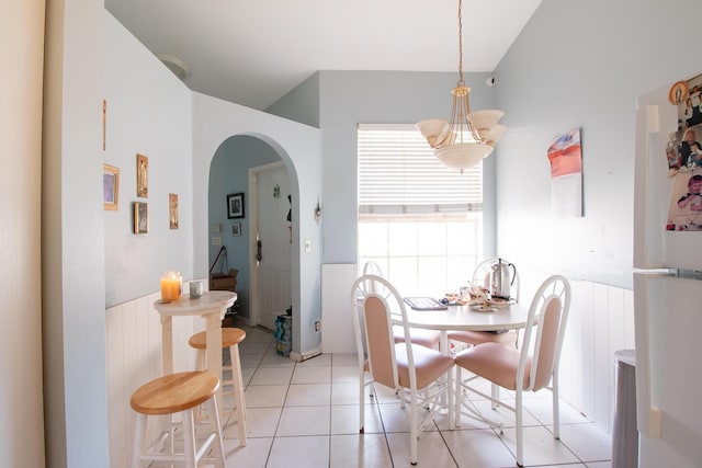 dining room featuring arched walkways, light tile patterned floors, vaulted ceiling, and wainscoting