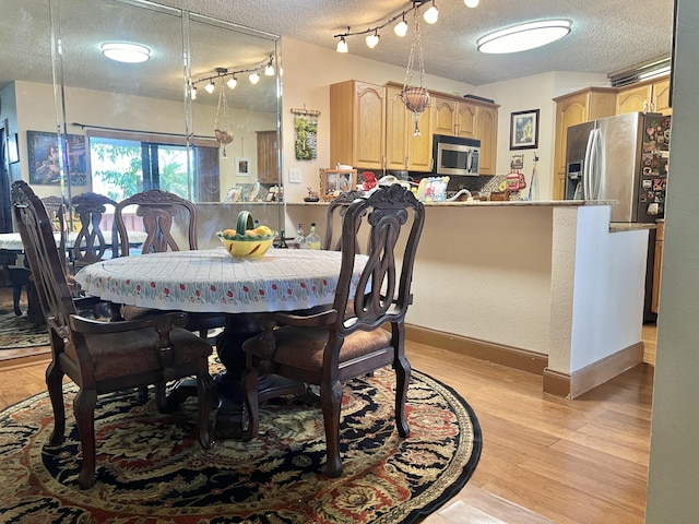 dining area featuring a textured ceiling, baseboards, rail lighting, and light wood-style floors