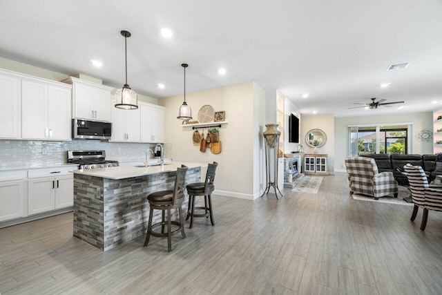 kitchen with pendant lighting, an island with sink, white cabinets, and appliances with stainless steel finishes