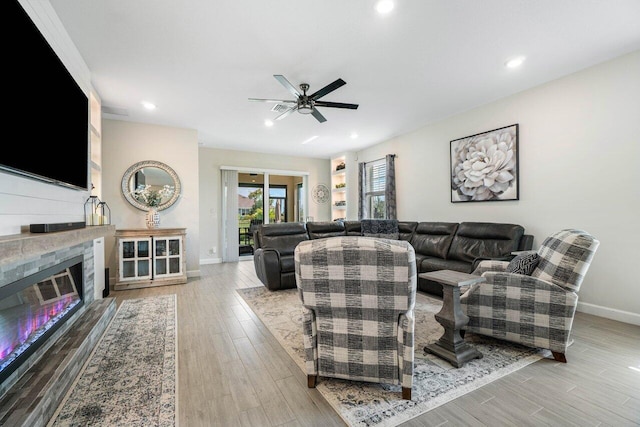 living room featuring ceiling fan, a fireplace, and light hardwood / wood-style floors