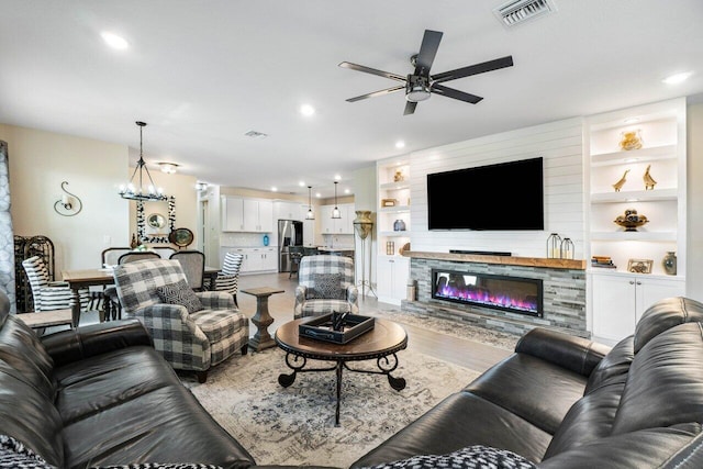 living room with hardwood / wood-style flooring, a fireplace, built in features, and ceiling fan with notable chandelier