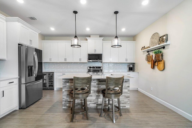 kitchen with a breakfast bar, appliances with stainless steel finishes, pendant lighting, a kitchen island with sink, and white cabinets