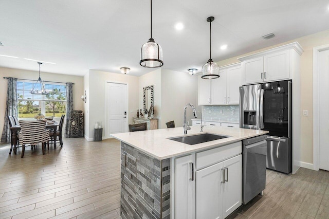 kitchen with sink, white cabinetry, tasteful backsplash, appliances with stainless steel finishes, and a kitchen island with sink