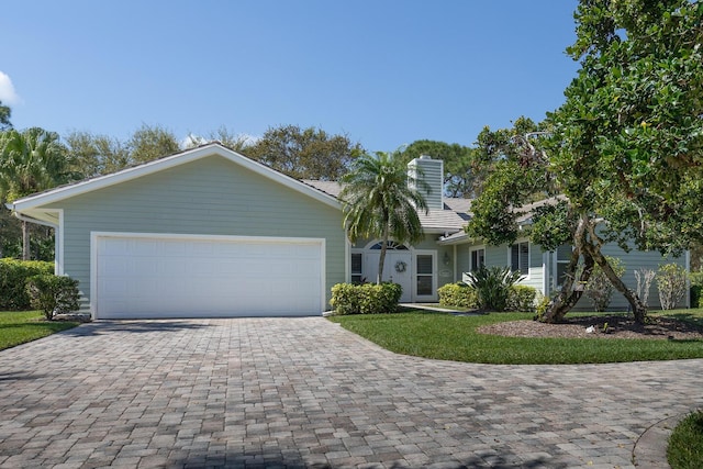 view of front of property featuring an attached garage, a chimney, a front lawn, and decorative driveway