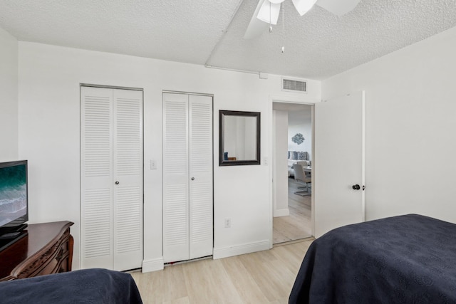 bedroom featuring ceiling fan, multiple closets, light wood-type flooring, and a textured ceiling