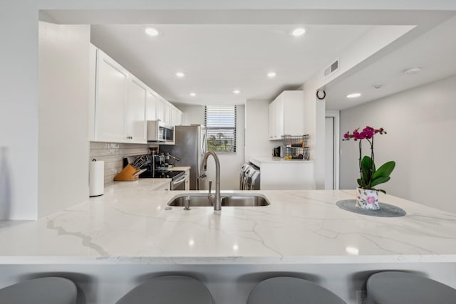 kitchen featuring sink, kitchen peninsula, stainless steel appliances, and light stone counters