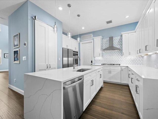 kitchen featuring white cabinetry, sink, a kitchen island with sink, stainless steel appliances, and wall chimney range hood