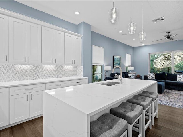 kitchen featuring a kitchen island with sink, sink, hanging light fixtures, and white cabinets