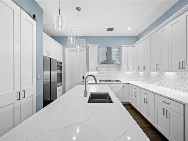 kitchen featuring sink, white cabinetry, pendant lighting, decorative backsplash, and wall chimney range hood