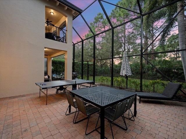 patio terrace at dusk with ceiling fan, a balcony, and glass enclosure