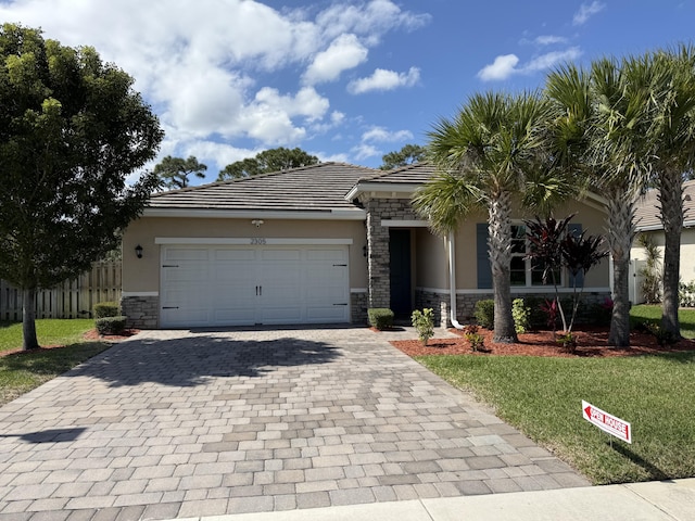 view of front of house featuring decorative driveway, stucco siding, a front yard, a garage, and stone siding