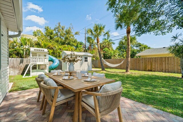 view of patio with a fenced backyard, an outbuilding, a storage unit, a playground, and outdoor dining space