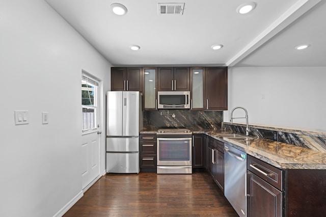 kitchen featuring sink, dark stone countertops, stainless steel appliances, dark hardwood / wood-style flooring, and decorative backsplash