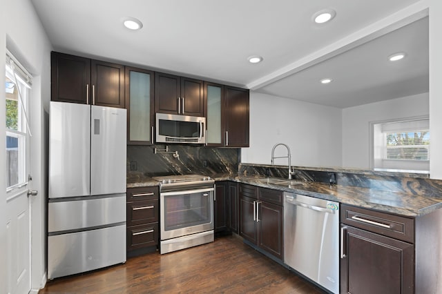 kitchen featuring appliances with stainless steel finishes, dark hardwood / wood-style floors, dark stone countertops, kitchen peninsula, and a healthy amount of sunlight