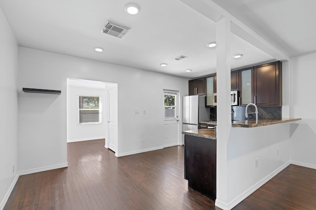 kitchen featuring dark hardwood / wood-style flooring, decorative backsplash, dark brown cabinetry, kitchen peninsula, and stainless steel appliances